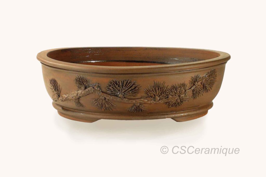 Ce superbe pot pour bonsaï de forme ovale est une pièce unique. Le motif représentant une branche de mélèze, a été entièrement sculpté à la main. Disponible dans la boutique en ligne.